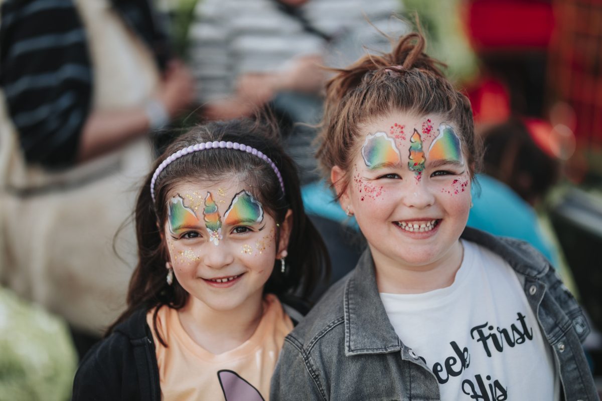 Zwei junge Mädchen lachen in die Kamera. In ihren Gesichtern sind Schmetterlinge mit Kinderschminke gemalt.