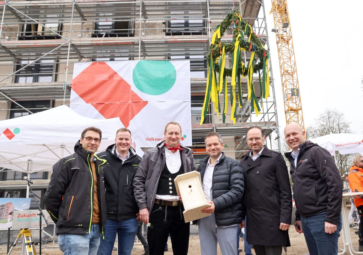 Sechs Männer stehen vor einem Richtkranz und das Modernisierungsprojekt ist im Hintergrund zu sehen.