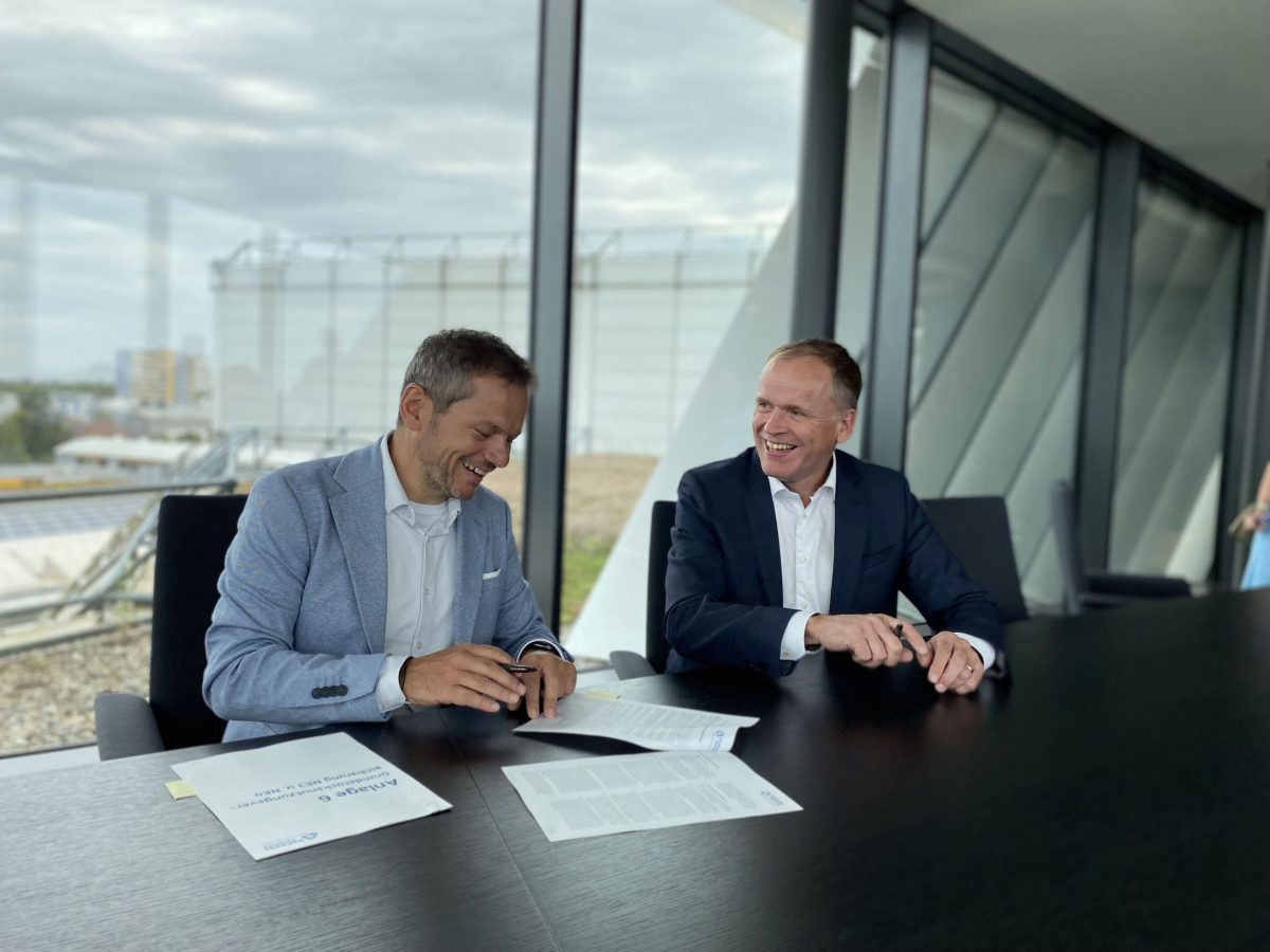 Zwei Männer sitzen an einem Tisch und unterzeichnen einen Vertrag.