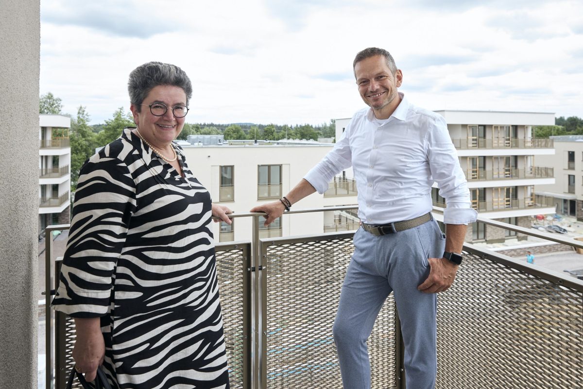Zwei Personen stehen auf einem Balkon mit dem Quartier im Hintergrund.