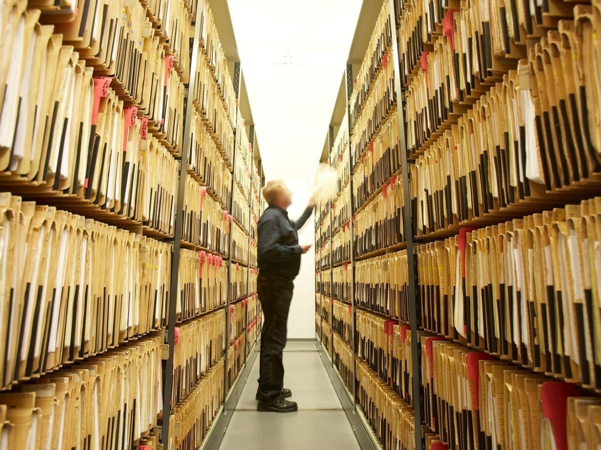 Ein Mann steht zwischen zwei großen Regalen voller Akten.