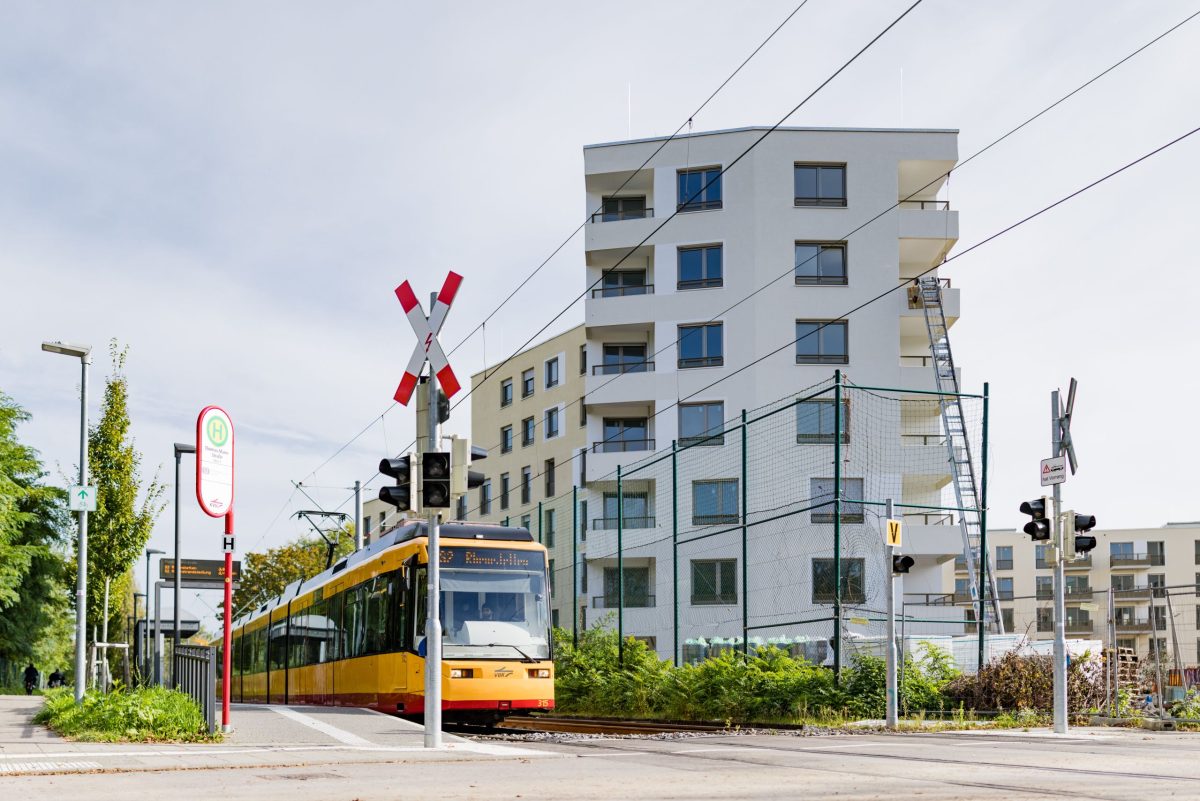 Eine Straßenbahn an der Haltestelle, im Hintergrund ein Gebäude vom August-Klingler_Areal in Karlsruhe Daxlanden.