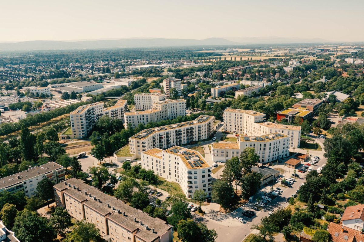 Luftaufnahme eines Wohnquartiers der Volkswohnung mit mehreren hellen Mehrfamilienhäusern, begrünten Dächern und umliegenden Wohn- und Gewerbegebieten.