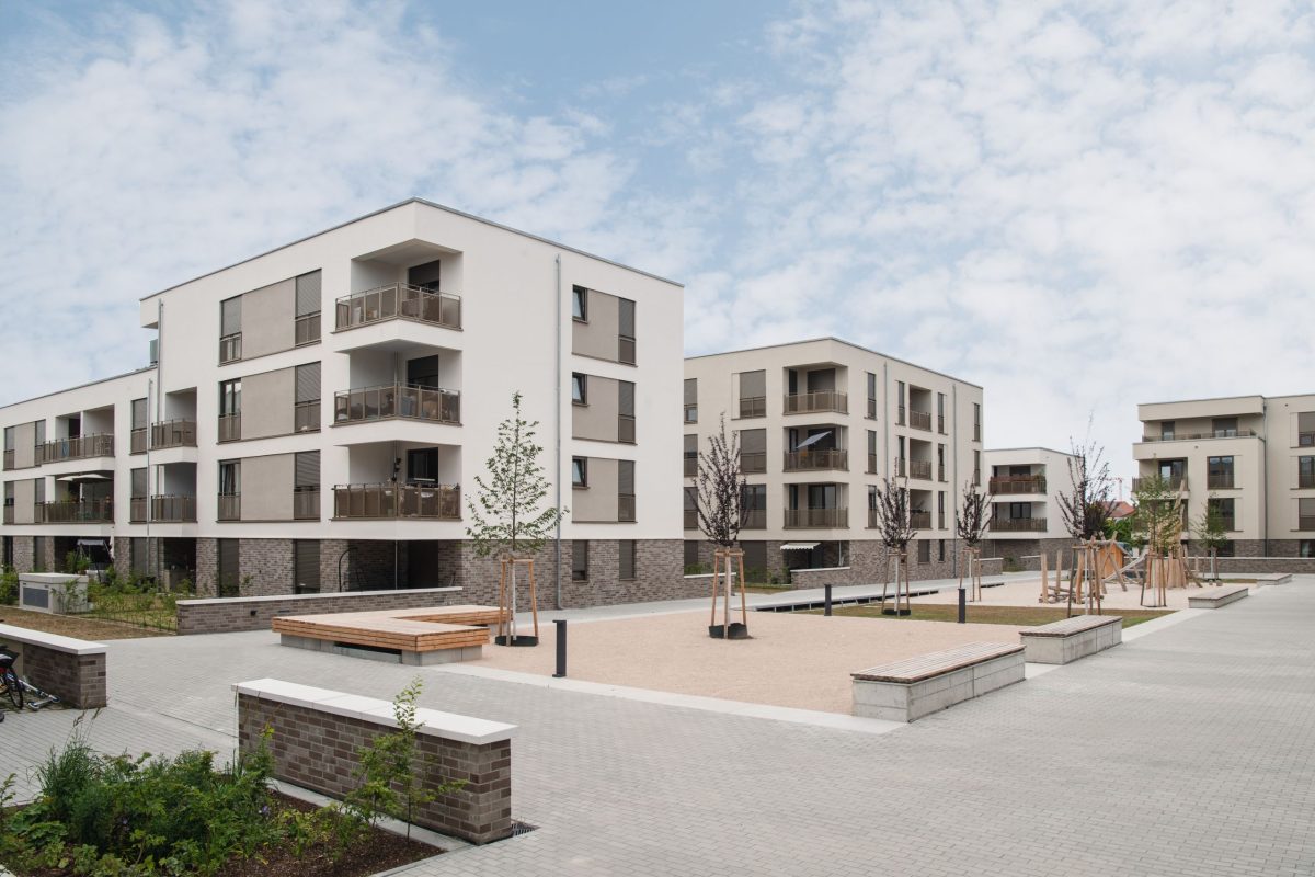 Moderne Mehrfamilienhäuser im Wohnpark Mittendrin der Volkswohnung mit Balkonen, begrüntem Innenhof, Sitzgelegenheiten und jungen Bäumen.