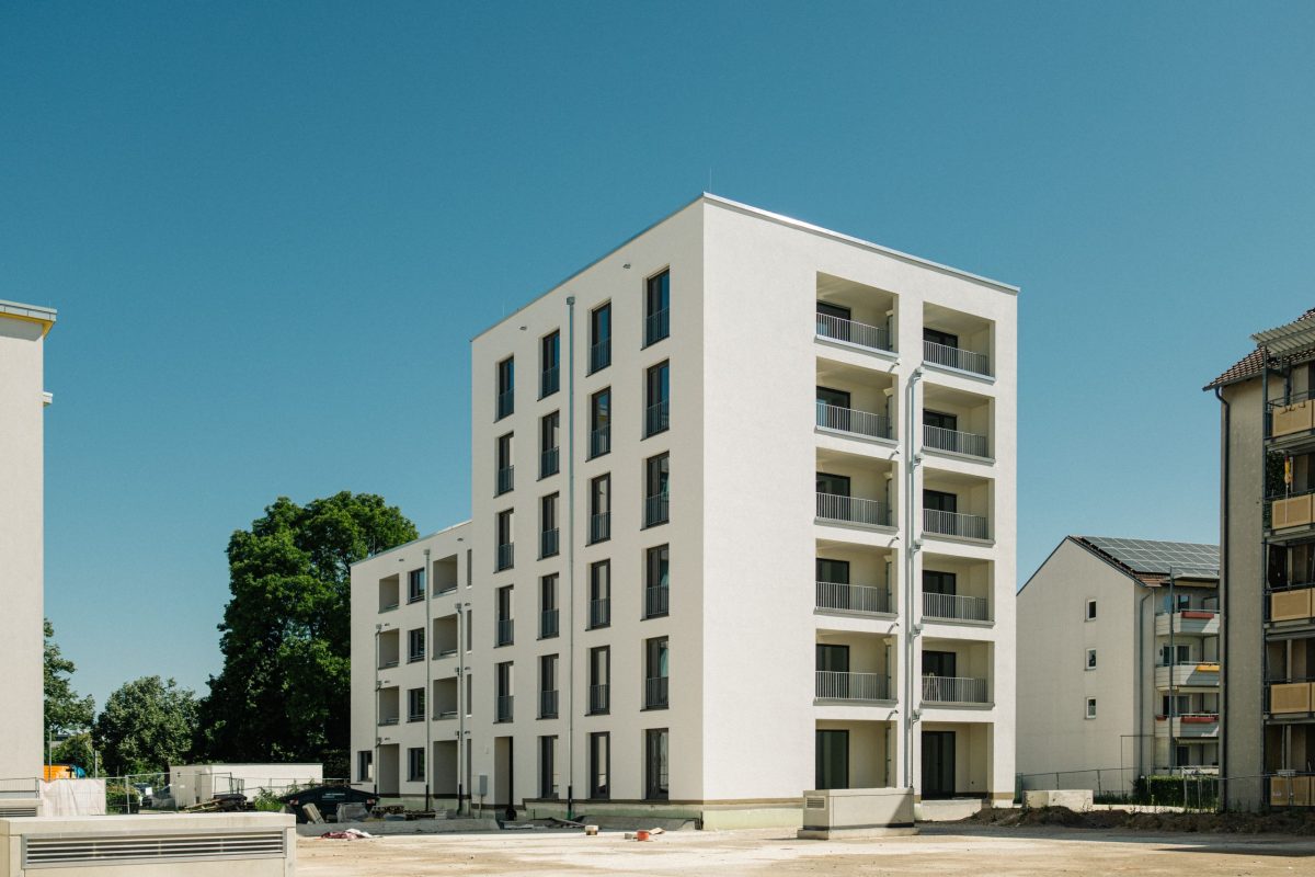 Modernes helles Mehrfamilienhaus der Volkswohnung mit mehreren Etagen und Balkonen vor blauem Himmel.